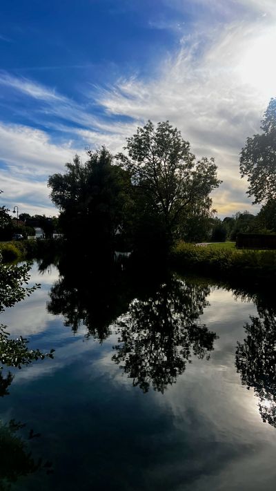Still canal in Olching reflecting trees and a streaked sky