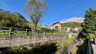 Arabba village stream, chalets, and a pale peak in morning light