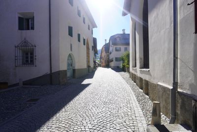 Sunlit cobblestone street between white houses